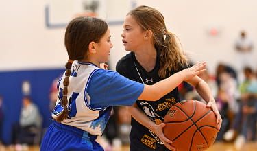 Two girls playing basketball, one holding the ball while the other defends.