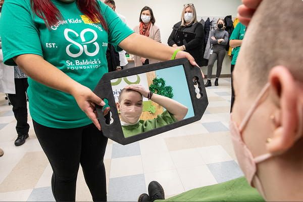 Person getting their head shaved looks at their reflection in a mirror.