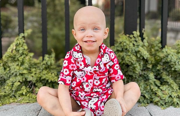 Lilah sitting outdoors, smiling and wearing bright red Hello Kitty pajamas.