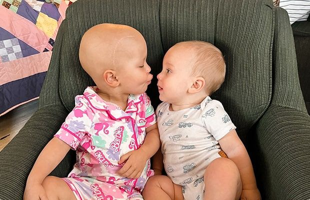 Lilah and her baby brother sitting together on a chair, facing each other.