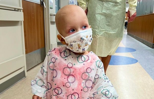 Lilah wearing a mask and hospital gown while walking in a hospital hallway.