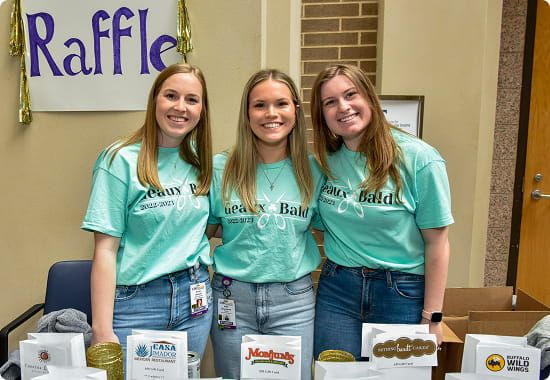 Three volunteers stand behind a raffle table at a community fundraising event.