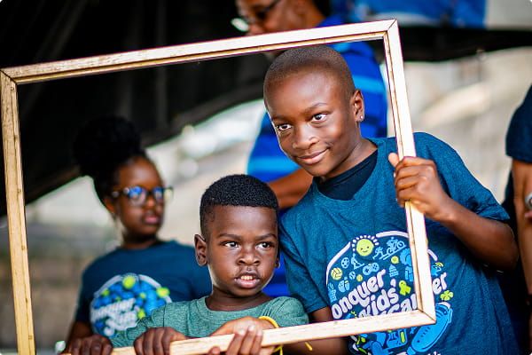 Two children holding an empty wooden frame pose together at a St. Baldrick’s Foundation event.