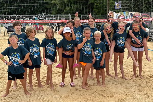 Kids and teens posing together on a sand volleyball court.