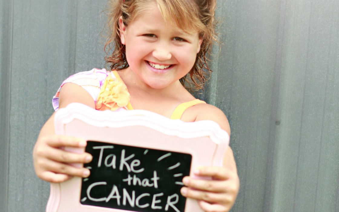 Chloe holding a sign that reads, 'Take that, cancer'