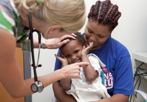 Khalid squirms and smiles in his mother's lap as a doctor examines him