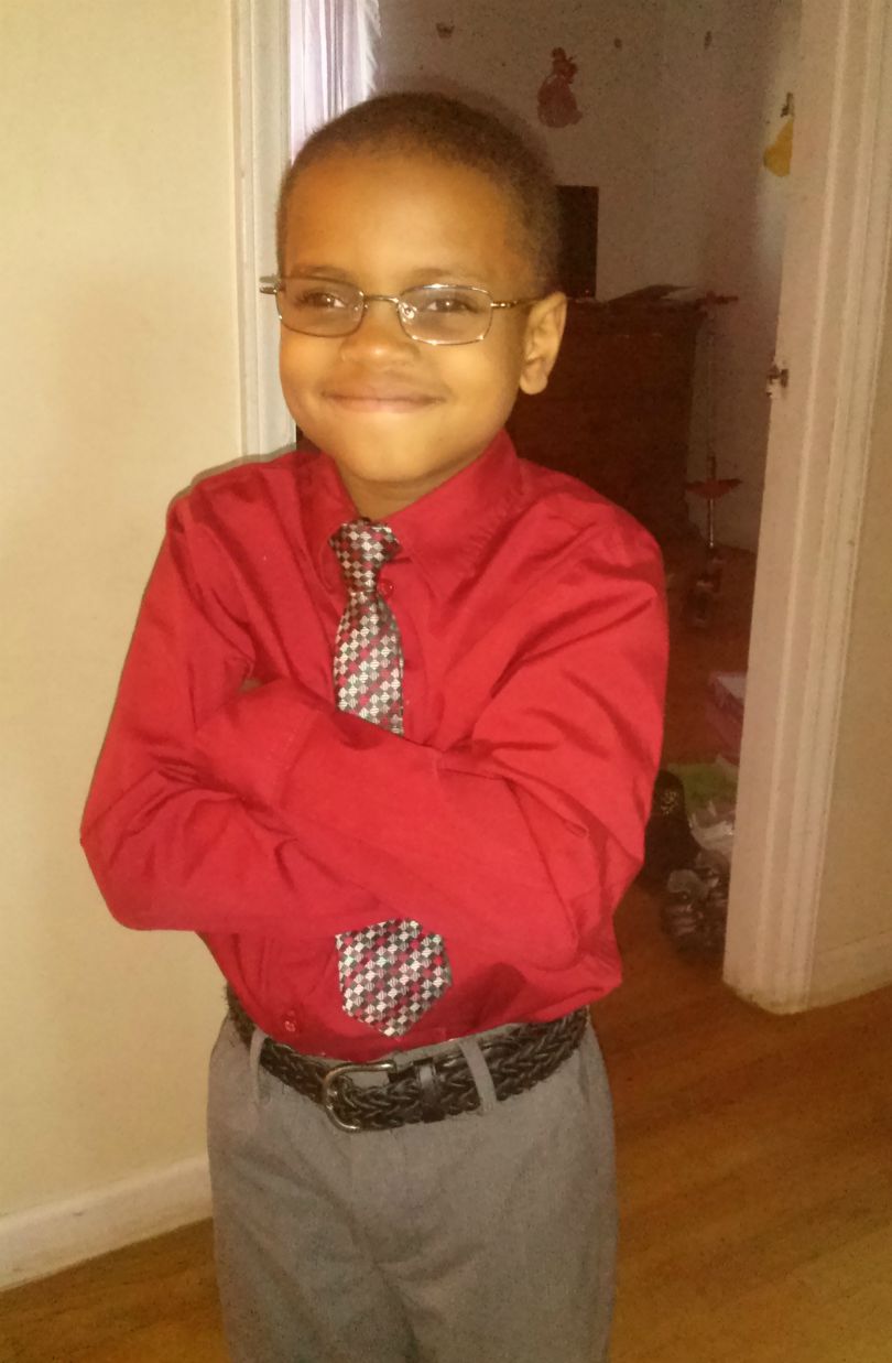 Khalid smiles and crosses his arms in a red shirt with a tie