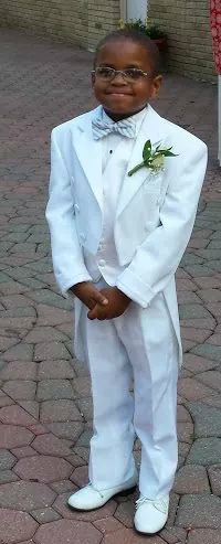 Khalid stands and smiles while dressed in a white suit