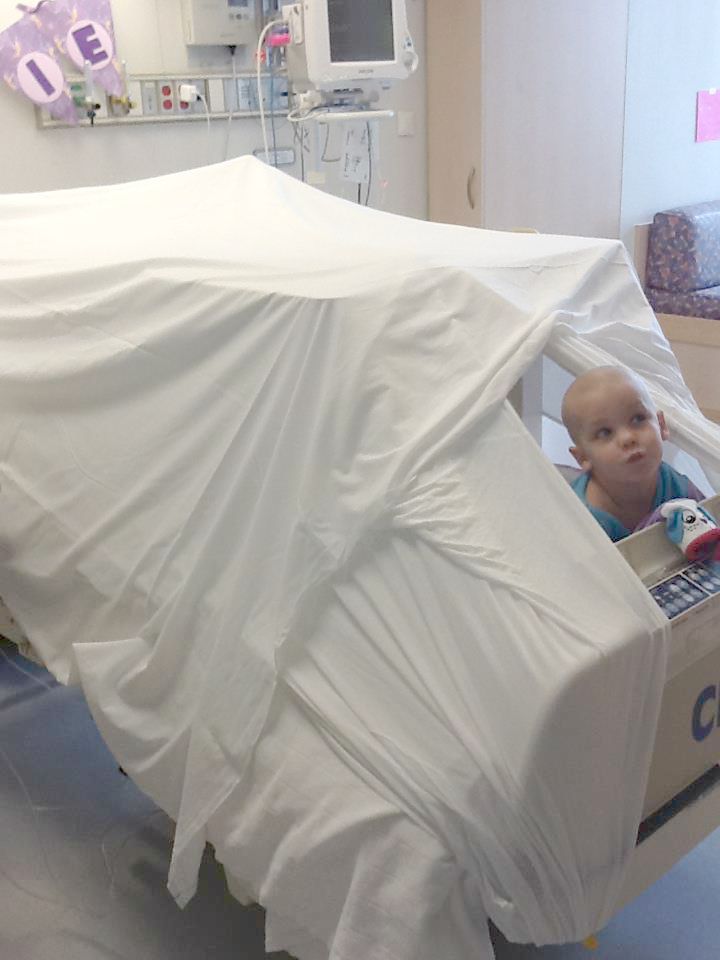 Roxie peers out of a fort made on her hospital bed