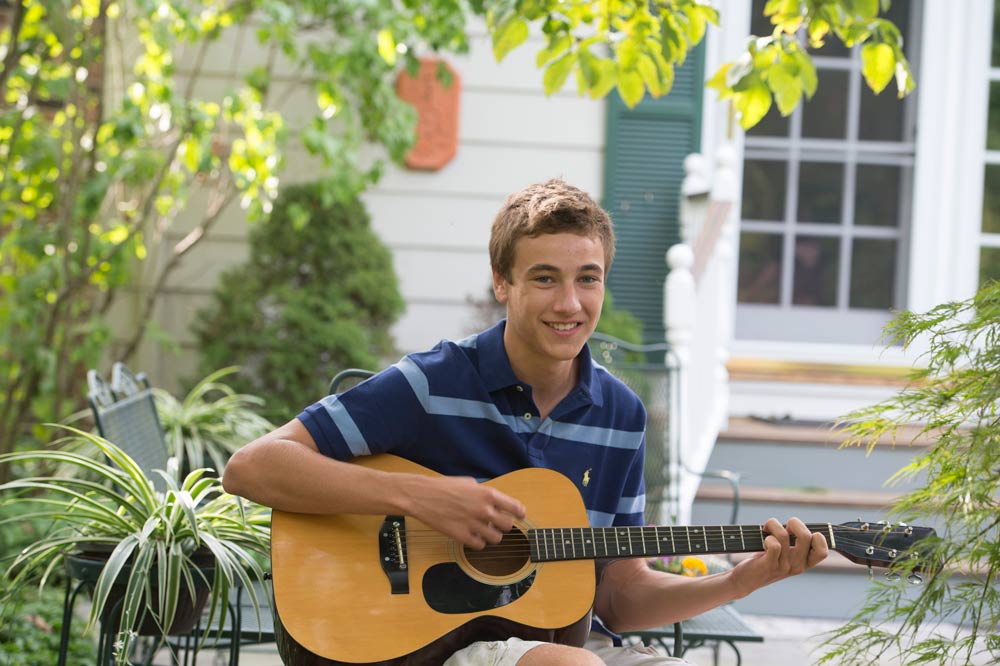 Aaron plays his guitar while smiling in the summer sun