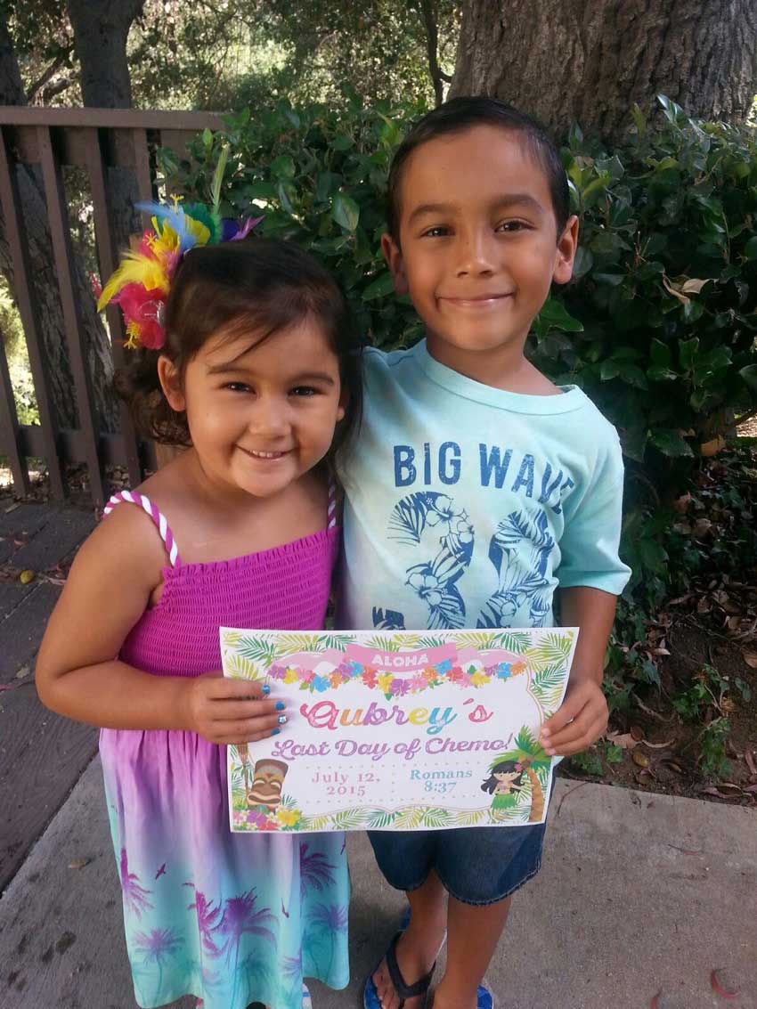 Aubrey and her brother joyfully holding a sign signifying her last day of chemo