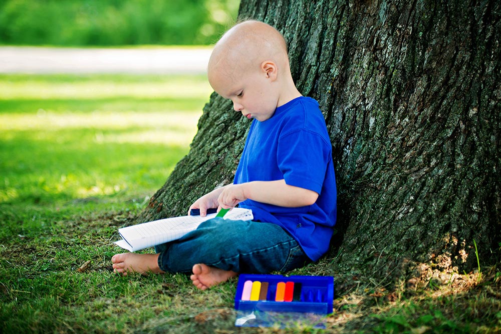 Chase sits under a tree and colors in a notebook