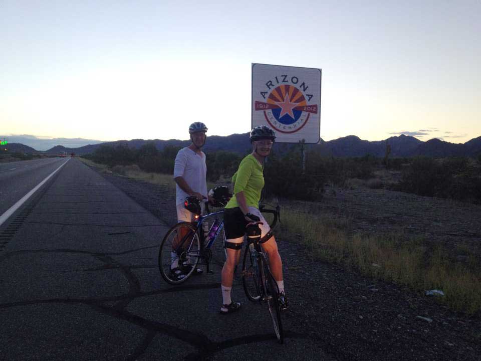 Kim and Jon pose for a photo with a sign at the Arizona border