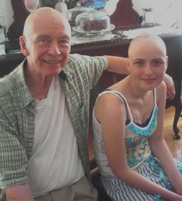 Grandfather sits with granddaughter, both bald, while she was in treatment for osteosarcoma