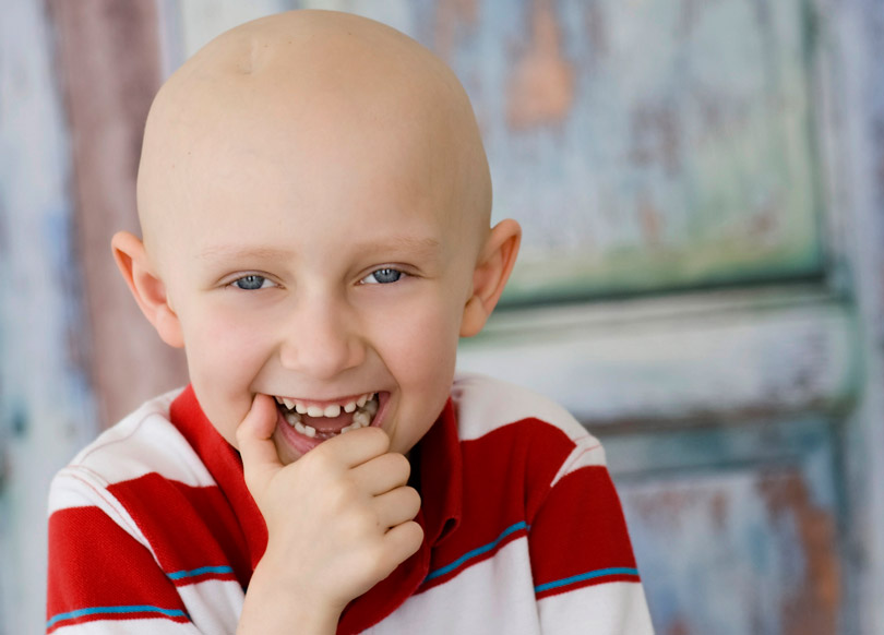 Sam, bald from treatment for medulloblastoma, smiles at the camera.