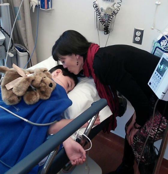 Addison's mom leans over his hospital bed to give him a kiss