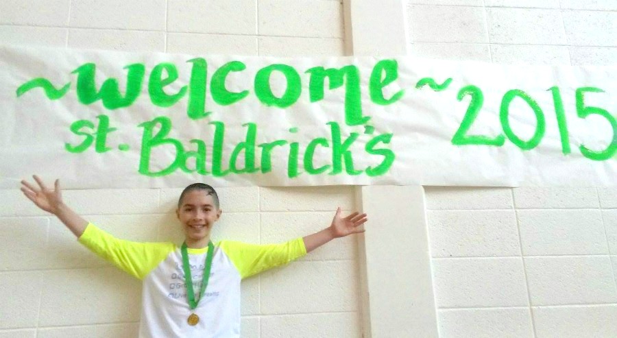 Addison spreads his arms underneath a sign advertising the St. Baldrick's event
