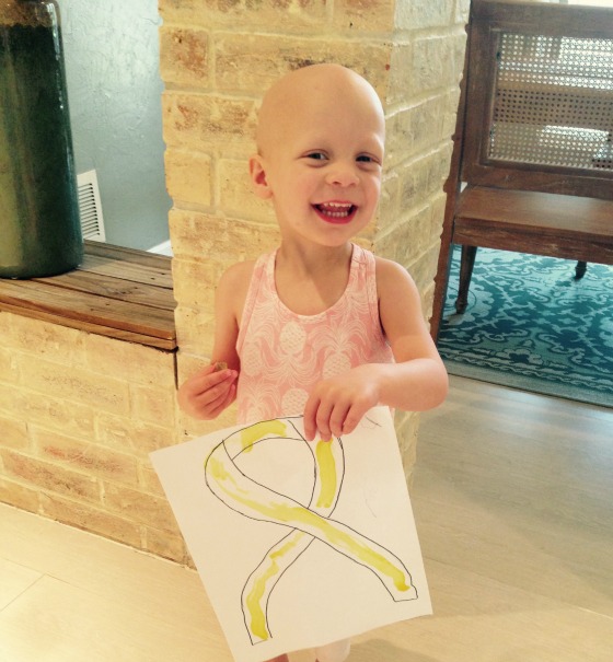 Avery holds a sign depicting a gold ribbon for childhood cancer awareness