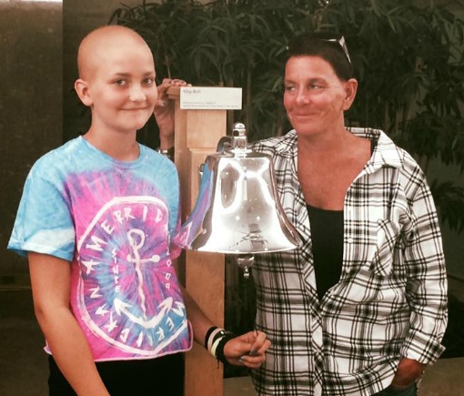 Daphne and her mom stand next to the bell that signals the end of treatment