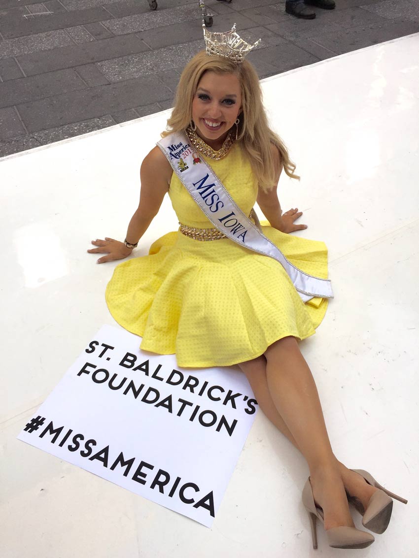 Miss Iowa sitting on the ground with her crown and sash on