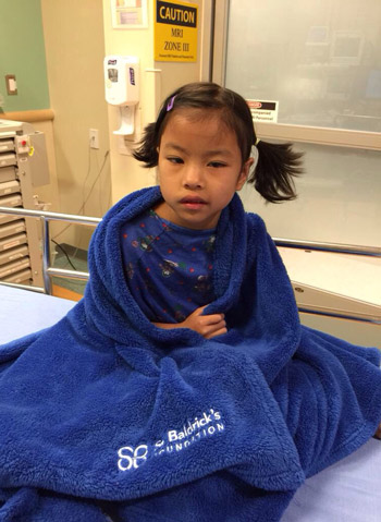 Daisy wrapped in a blue St. Baldrick's blanket before her MRI