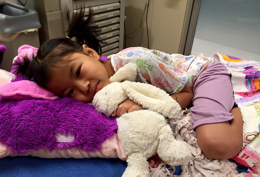 Daisy lying in a hospital bed cuddling a stuffed bunny