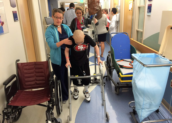 Luke walks the hospital halls with the aid of a walker and a nurse