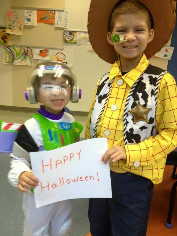 Julian and Brayden, dressed as Buzz Lightyear and Woody, hold a sign that says: Happy Halloween