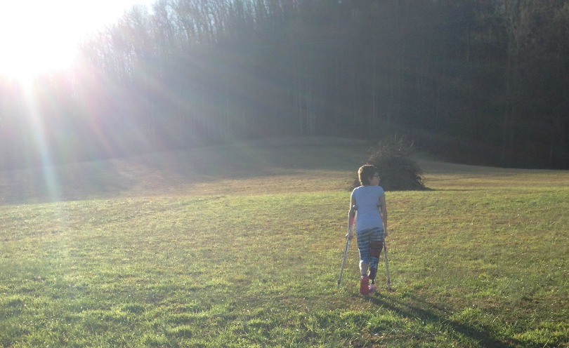 Elise walks through a field on her prosthetic and her crutches