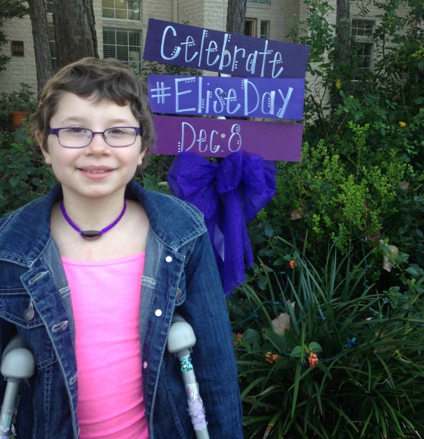 Elise smiles at the camera in front of a sign proclaiming 'Elise Day'