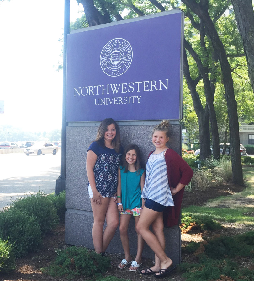 Sara and her sisters pose next to a Northwestern University sign