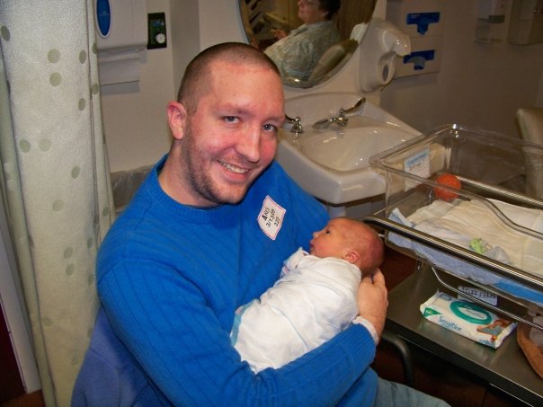 Collin, sans eyebrows, holds his newborn child